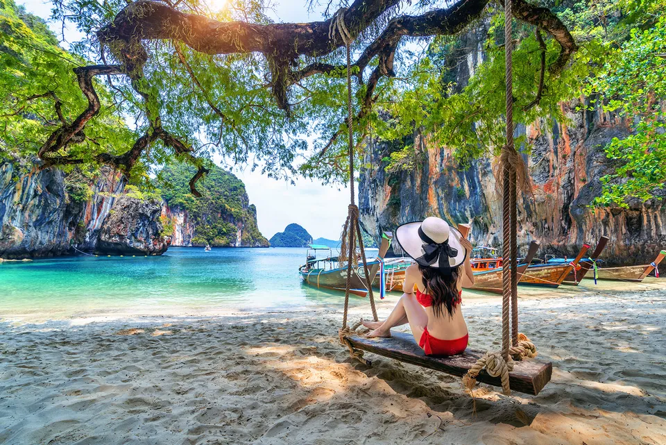 A tropical Phuket beach with turquoise water, long-tail boats and limestone cliffs